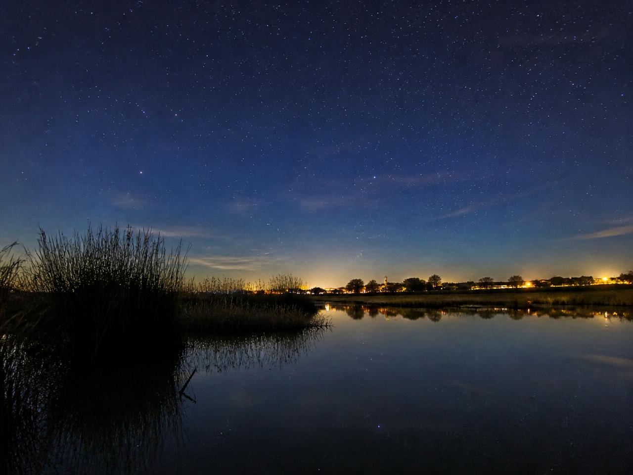 Sternenhimmel über den Salzwiesen der Camargue mit den Lichtern des Dorfes in der Ferne